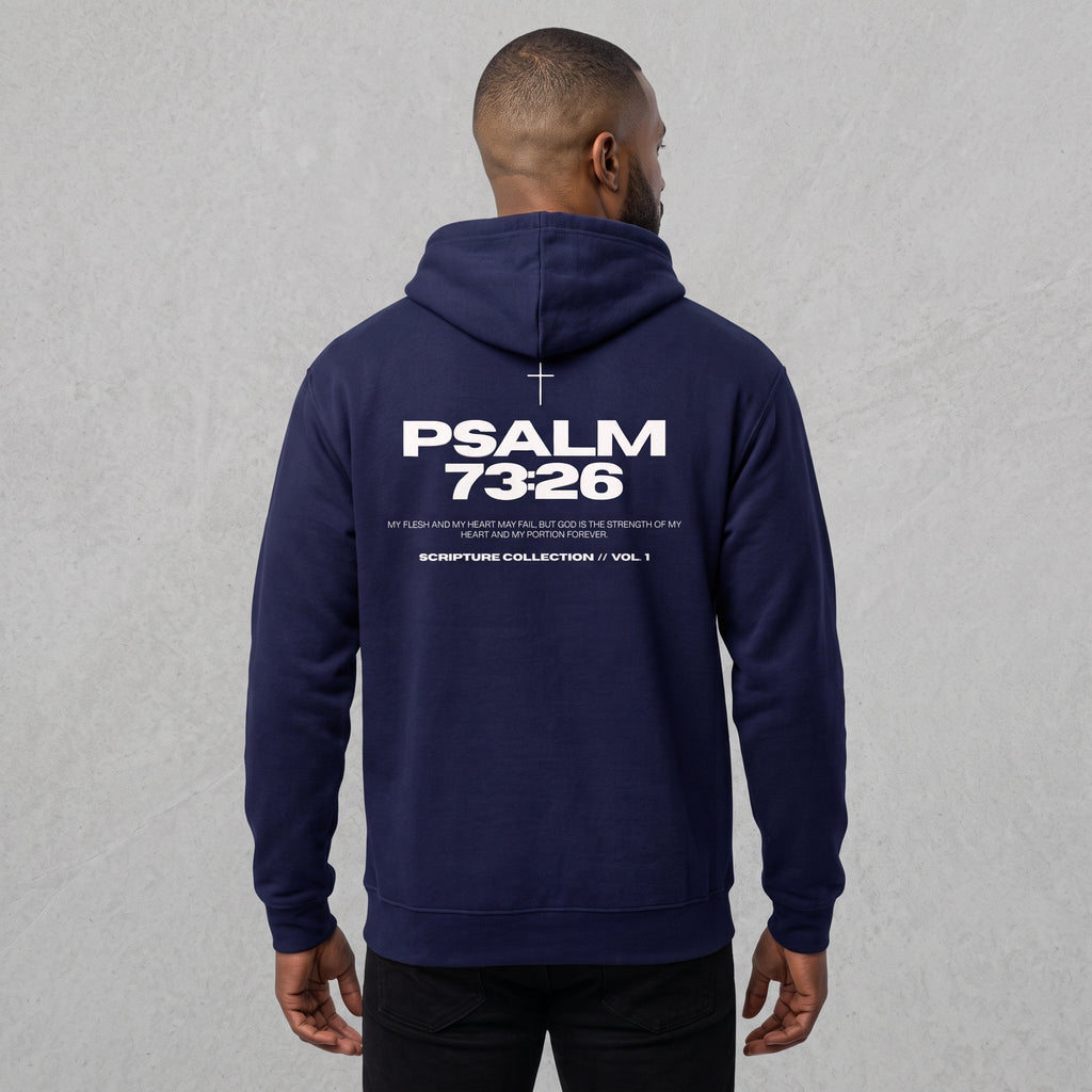 A man viewed from the back wearing a navy blue hoodie with 'PSALM 73:26' printed in white on the back, set against a textured light gray wall.