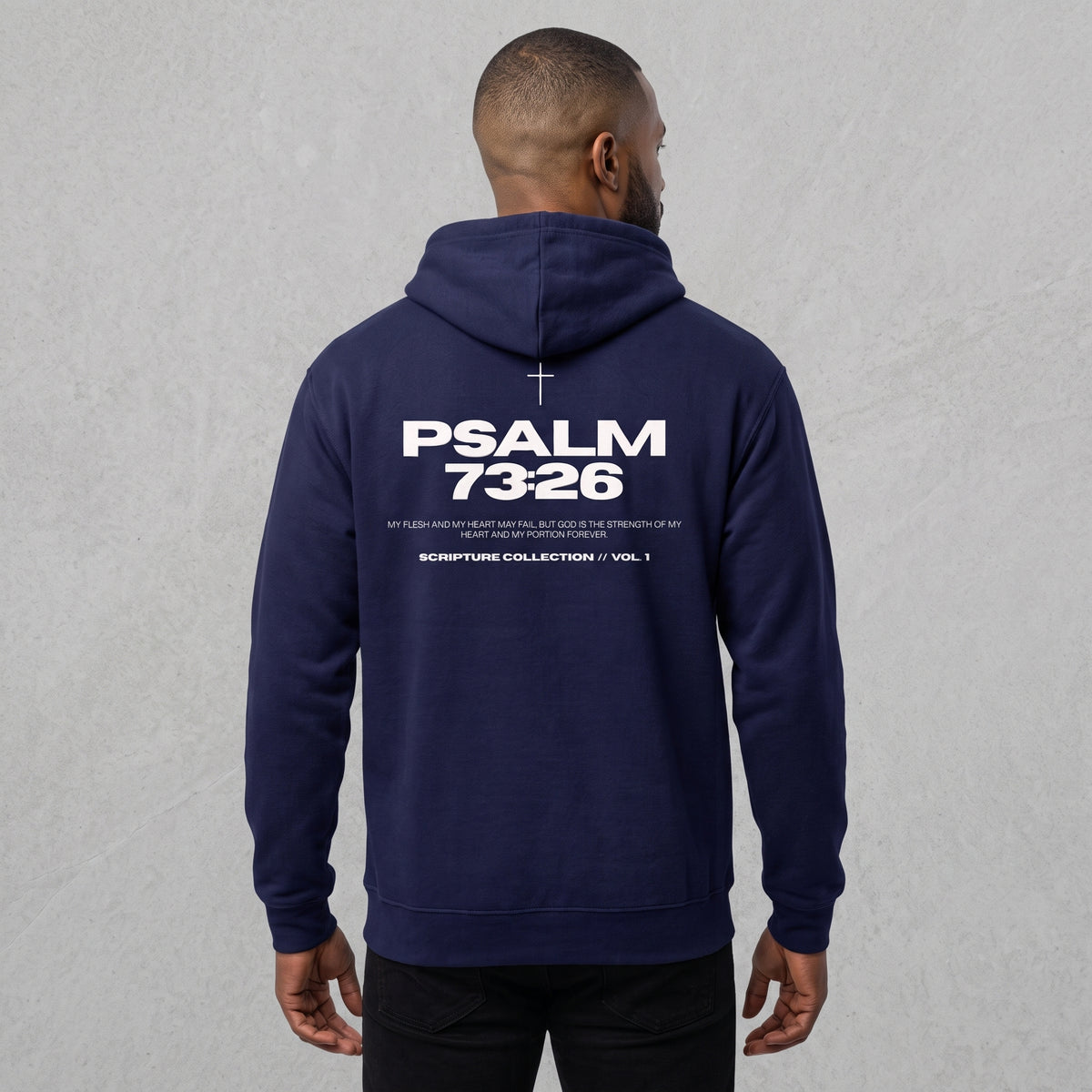 A man viewed from the back wearing a navy blue hoodie with 'PSALM 73:26' printed in white on the back, set against a textured light gray wall.