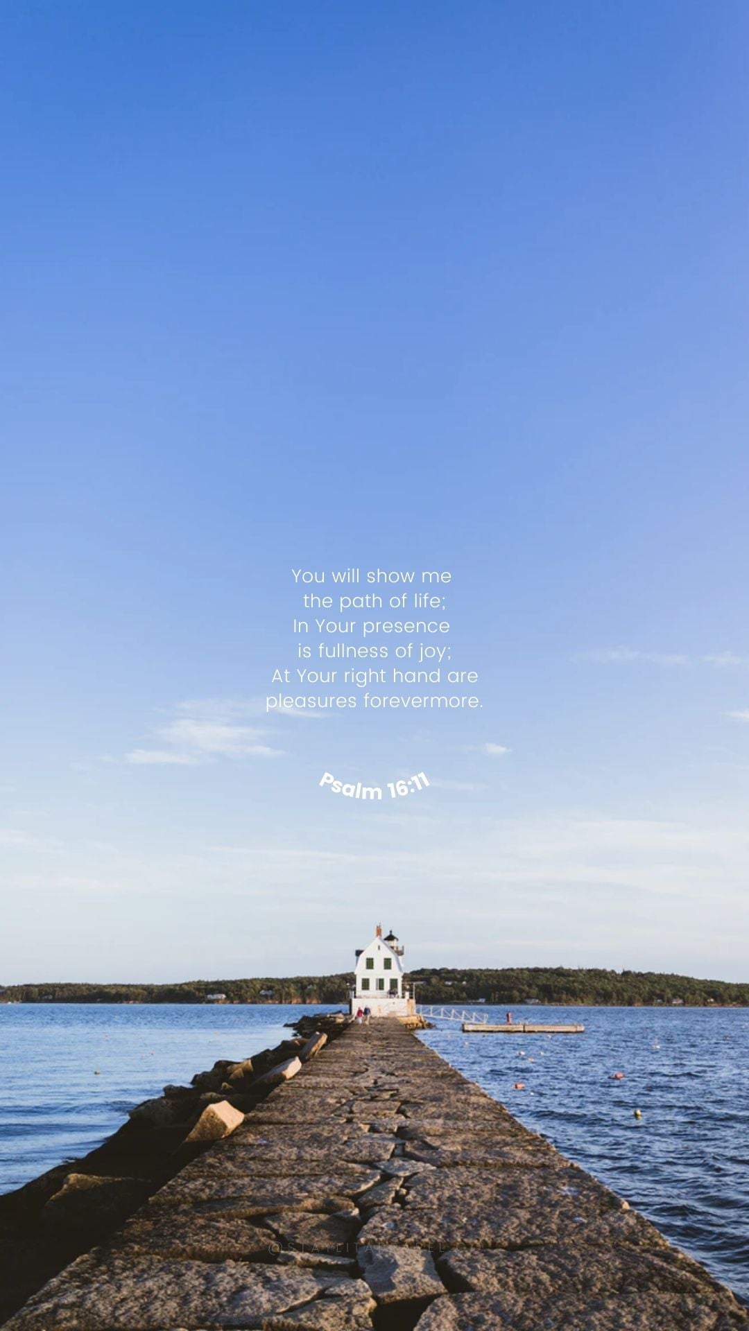 Lighthouse on a pier extending into the ocean with a clear blue sky.
