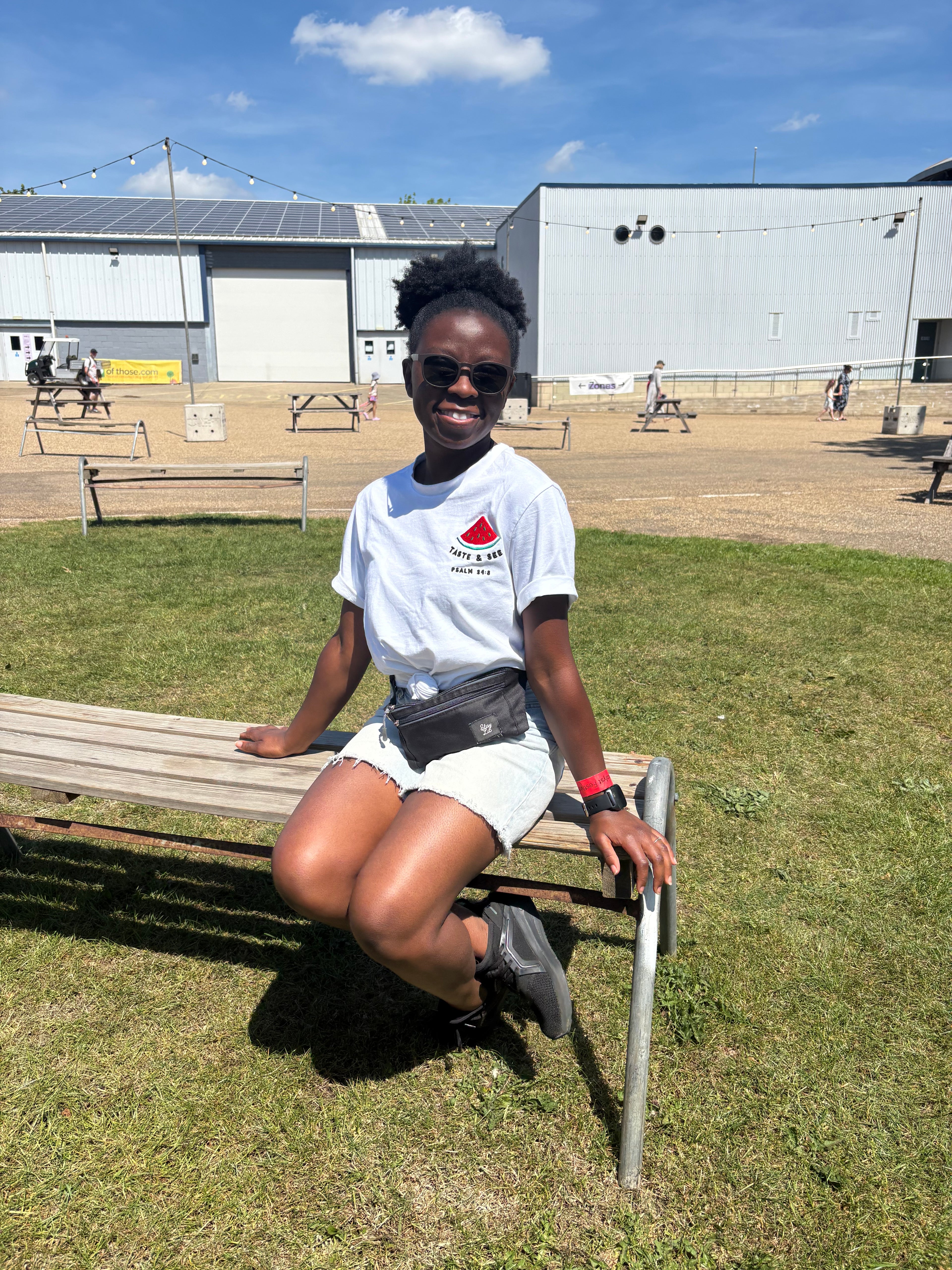 Person sitting on a bench in an outdoor setting with a building and clear sky in the background